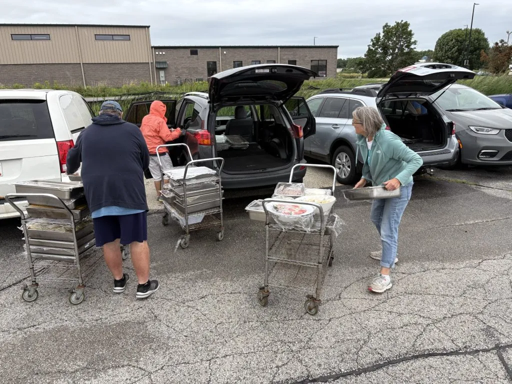 People loading trunk of vehicle with trays of food