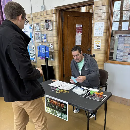 man sitting at table talking to other man standing