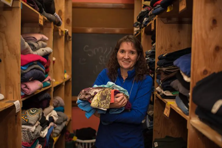 woman holding stack of clothing in clothing donation closet
