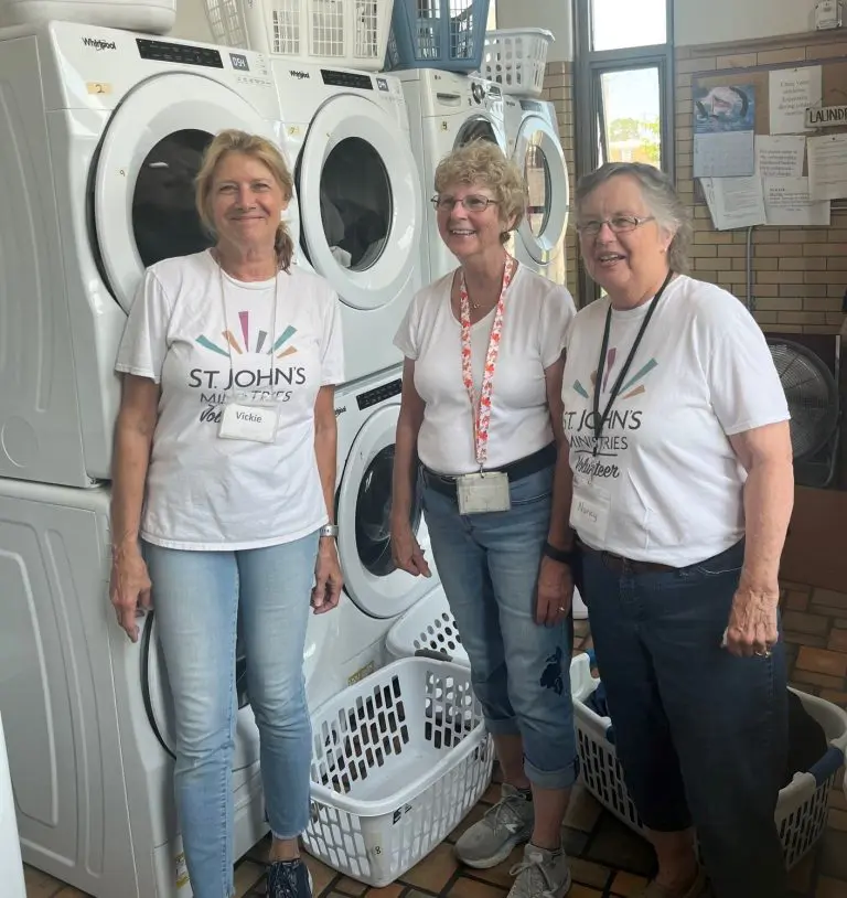 3 women standing in front of stacks of washing machines