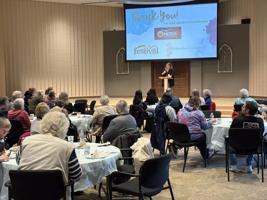 people sitting at table watching someone speak at a podium